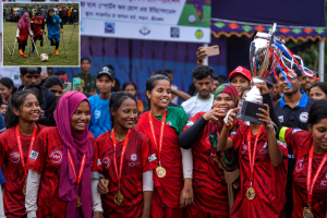 A group of young women with disabilities in red football jerseys celebrate with medals and a trophy at a sports event in Cox’s Bazar, Bangladesh, while an inset image shows Yasmin and Jasmin playing amputee football with crutches, highlighting disability inclusion and climate action.